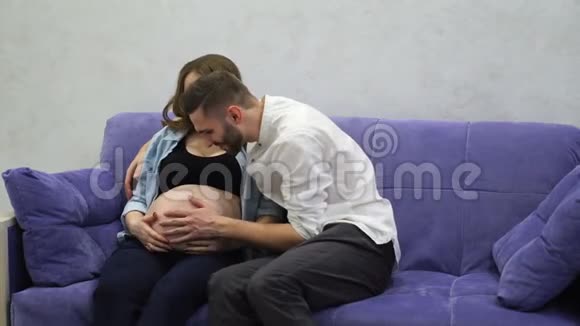 幸福的一对夫妻坐在家里笑着拥抱在一起女人怀孕了男人和婴儿交流视频的预览图