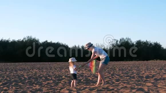 戴着帽子的金发美女妈妈和女儿在海滩上放风筝视频的预览图