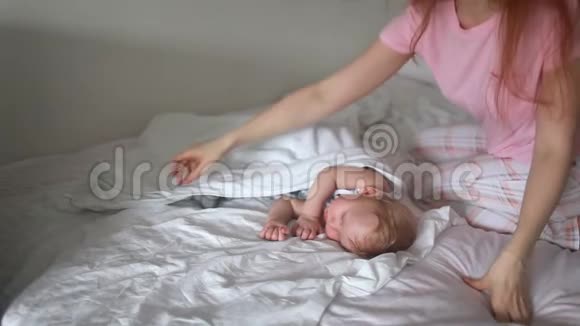 美丽的年轻妈妈和她可爱的小宝宝睡在家里的床上的侧面景色视频的预览图