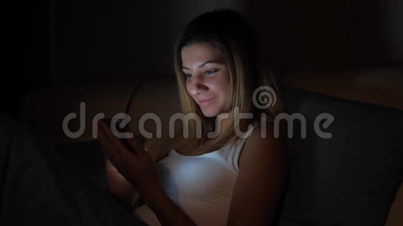在黑暗的微笑中女人使用手机晚上躺在床上视频的预览图
