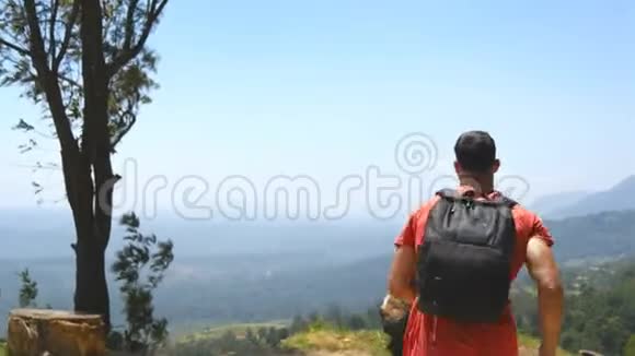 一个背着背包的年轻人爬上山顶举起双手男性游客站在美丽的边缘视频的预览图