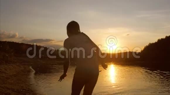 小女孩跑到日落的海滩上从脚下泼水慢镜头射击视频的预览图