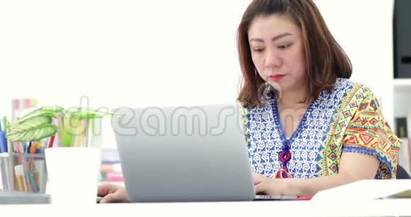 年轻的亚洲女商人在家里用笔记本电脑工作亚洲女人下班后伸展自己视频的预览图