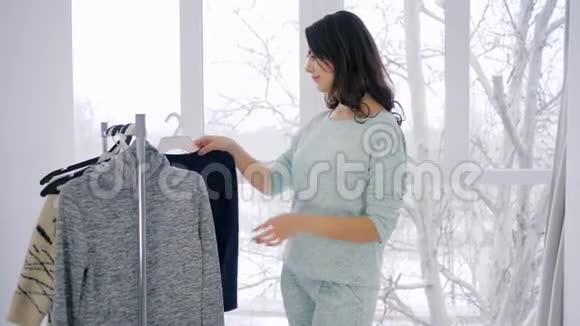 衣柜设计师的衣服可爱的女性尝试服装衣架在明亮的房间视频的预览图