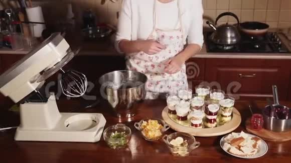 一个穿着厨房围裙的女人把甜奶油放在装有水果和浆果的眼镜里视频的预览图