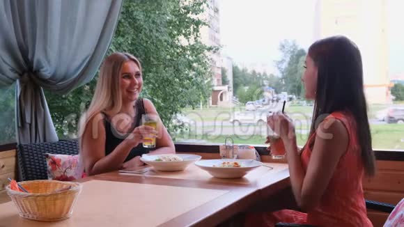 两个时髦的酷女孩朋友金发和黑发在咖啡馆喝鸡尾酒视频的预览图