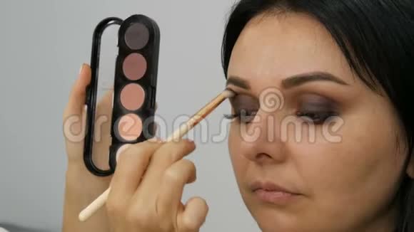 专业的眼妆化妆师在美容院用特殊的刷子给年轻女子化妆视频的预览图