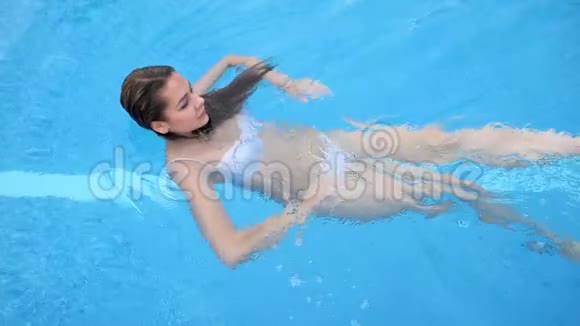 长头发的年轻女子身穿泳装夏天在游泳池的蓝水边休息视频的预览图