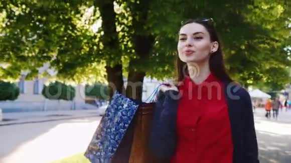 时髦的女人穿着一件红色的连衣裙带着购物袋迪尔在城里走来走去阳光明媚美丽的倒影在视频的预览图