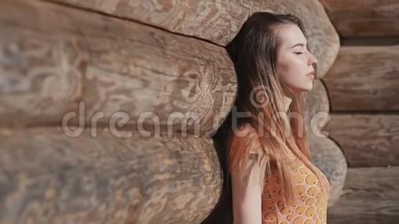 美丽性感的年轻女孩长发穿着一件裙子摆在一堵木墙附近从宽的原木放松一下夏季视频的预览图