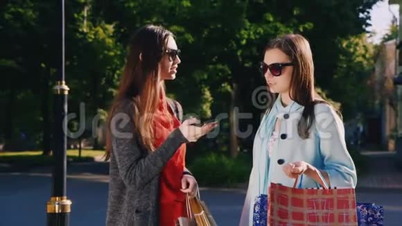 两个女朋友带着购物袋在户外使用智能手机视频的预览图