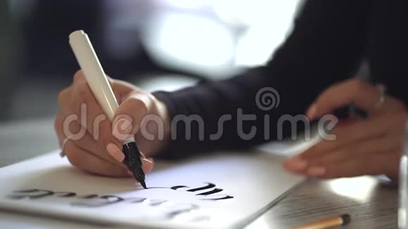 年轻女子的手坐在咖啡馆或工作室里在白纸上写着美丽的字体短语手写刻字视频的预览图