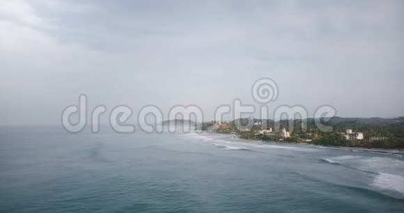 空中无人机飞越拍摄田园诗般的泡沫海浪到达壮丽的热带度假胜地海岸与建筑物视频的预览图