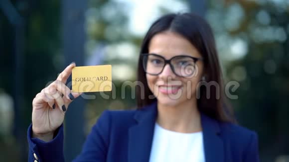 成功的美女在办公楼背景上对着镜头展示无限黄金信用卡视频的预览图