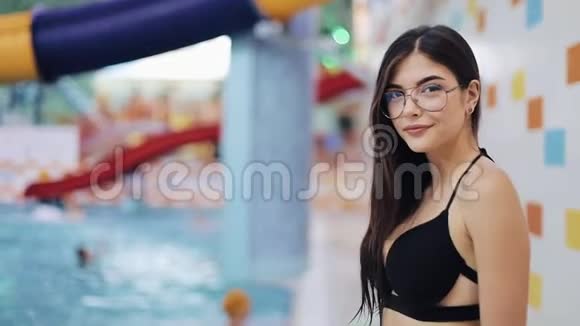 穿着黑色泳衣在游泳池里摆姿势的年轻女人在水上公园或游泳池中有魅力的女孩的肖像视频的预览图