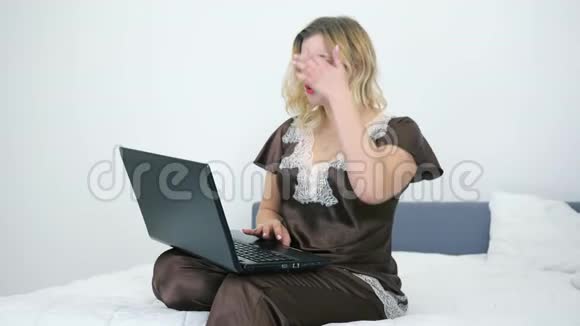 在线视频聊天漂亮的年轻女人在卧室里穿着睡衣在笔记本电脑上聊天视频的预览图