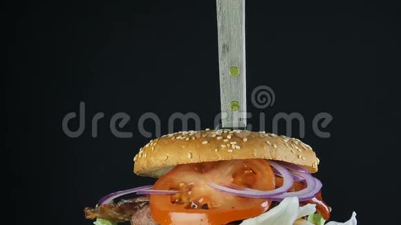 一个多汁的大汉堡有一个双面包和一个双切片上面有绿色和蔬菜用刀子钉在上面视频的预览图