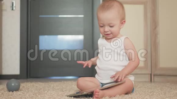 带着平板电脑的小男孩坐在家里的地板上在室内幼儿帅哥玩屏幕视频的预览图