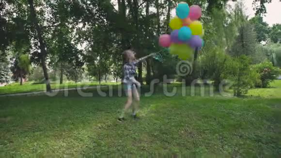 快乐的小女孩在公园里欢乐地旋转着五颜六色的气球视频的预览图
