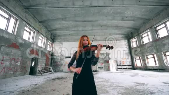 红发女士正在一座废弃的大楼里拉小提琴视频的预览图