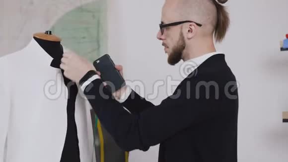 一位年轻的创意裁缝在他的工作室里的一个假人身上做一件白色夹克的尺寸用来缝制衣服有胡子的视频的预览图
