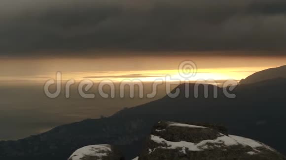 日落时分在雾中在深灰色的云层衬托下可以鸟瞰海边的山影射击迷人的视频的预览图