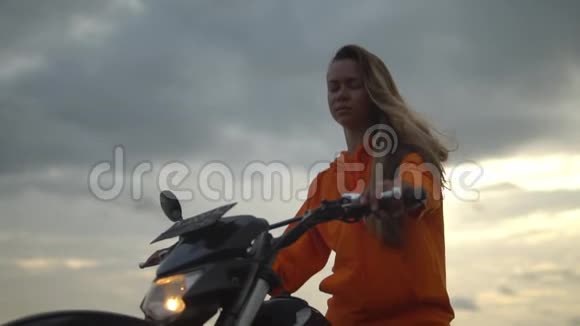 拍摄了波涛汹涌的大海和灰暗的夜空一个穿着橙色连帽衫的漂亮长发女孩骑着摩托车视频的预览图