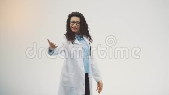 漂亮的年轻黑发医生穿着灰色背景的医疗服在这期间她身上有一个音筒视频的预览图