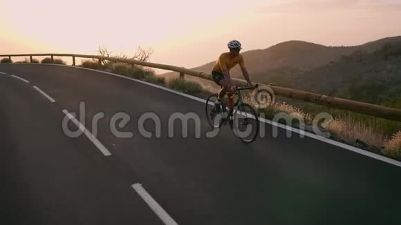一个戴着头盔和运动装备的职业自行车手在日落时分骑在蜿蜒的山上朝视频的预览图