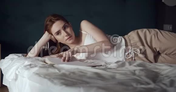 红头发的女人躺在床上放松看着她的日记视频的预览图