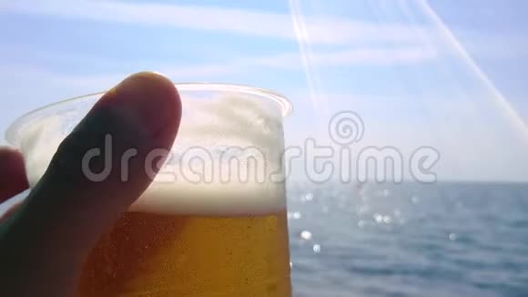 这只手拿着一个塑料玻璃和啤酒在海边视频的预览图