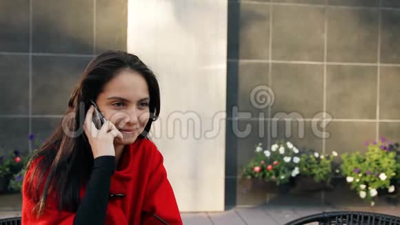 年轻的商务女士坐在街上一家咖啡馆的桌子旁用手机说话视频的预览图