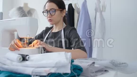 小企业和爱好概念年轻女性设计师的衣服在她的工作室里的缝纫机上工作视频的预览图