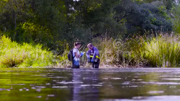 两位科学家穿着高橡胶靴站在森林河的水中视频的预览图