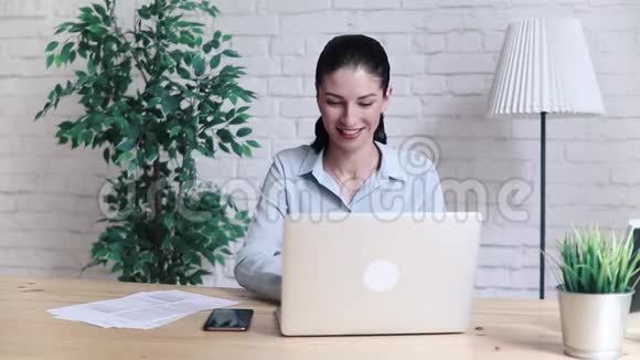 妇女在办公室的办公桌上使用笔记本电脑和智能手机视频的预览图