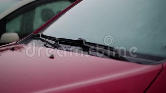 从外面看有大雨淋浴水滴落在汽车引擎盖上挡风玻璃上有雨刷的空红色汽车视频的预览图