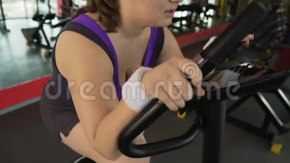 有动力的肥胖妇女在健身房的固定自行车上辛勤工作减肥视频的预览图
