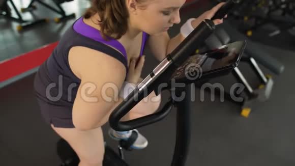 疲惫的超重妇女坐在固定的自行车上呼吸困难视频的预览图