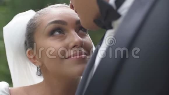 新郎在亲吻美丽的微笑新娘的头迷人的黑发女人正靠在他的鞋边视频的预览图