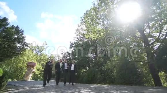 婚前散步英俊的新郎正积极地与他快乐的三个最好的男人交谈同时沿着花园散步慢慢视频的预览图