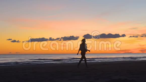 年轻女子在美丽的夕阳下快乐地走在海边视频的预览图
