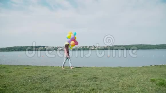 快乐的年轻女孩带着五颜六色的气球在湖岸散步4K视频的预览图