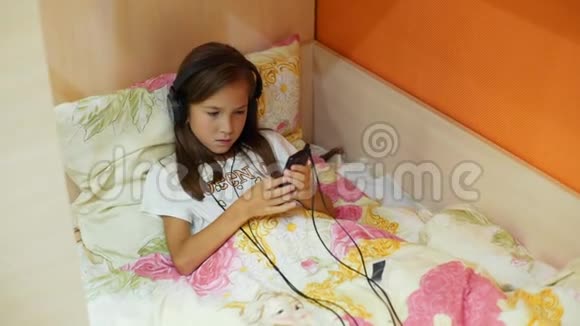 女孩8岁在耳机上听音乐那个女孩躺在床上戴着耳机视频的预览图