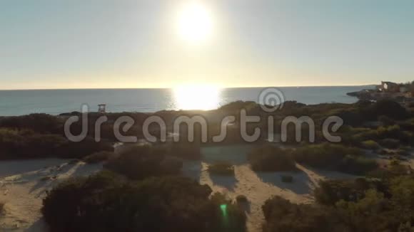 在阳光明媚的日子里用绿色灌木沙滩和小建筑在蓝天的衬托下俯瞰海岸线艺术视频的预览图