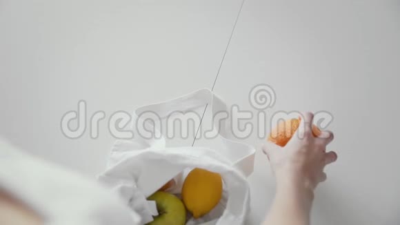 从她的肩膀上可以看到一个女人在厨房里用木制的苹果橘子和柠檬打开布料购物袋视频的预览图