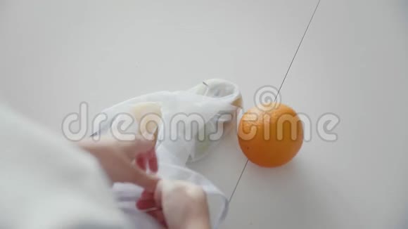 从她的肩膀上可以看到一个女人在厨房里用木制的苹果橘子和柠檬打开网状购物袋视频的预览图