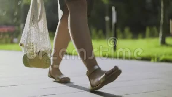 毛茸茸的腿的年轻女人拿着带蔬菜的棉网购物袋在夏季公园散步妇女权力视频的预览图