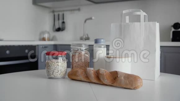 厨房木制桌子上有面包燕麦片荞麦牛奶蔬菜的未包装购物袋零垃圾家庭和视频的预览图