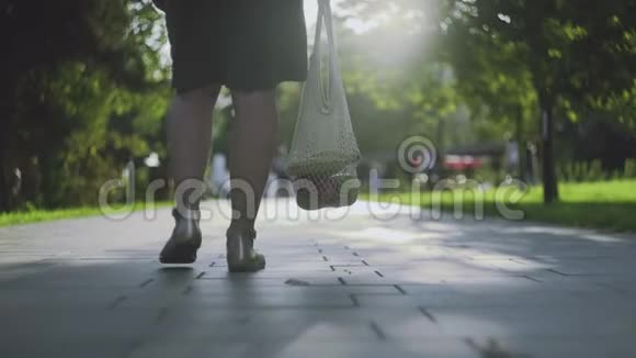 年轻女子拿着带蔬菜的棉网购物袋在夏季公园散步视频的预览图