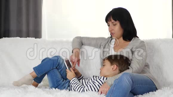 一位快乐的母亲和一个年幼的孩子在家里坐在沙发上的时候花时间吃平板电脑妈妈抱着儿子视频的预览图